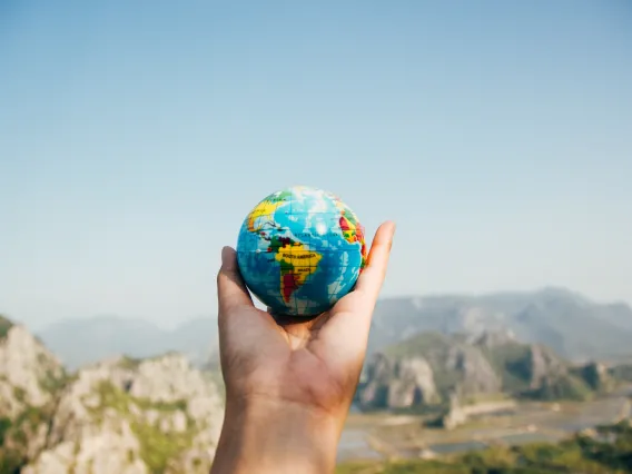 Mountain landscape with person's hand holding a globe