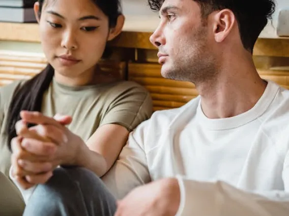 Couple sitting down holding hands with serious faces. 