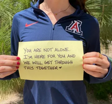 Woman holding sign saying, You are not alone. I am here for you and we will get through this together.